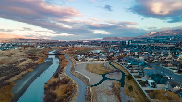 Morning sunrise cloudscape aerial hyperlapse above a river pathway trail and suburban community