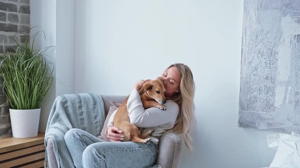 Young Beautiful Blonde Woman Caucasian Nationality Home Clothes Sits in a Cozy Armchair Hugging Her