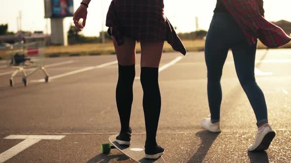 Back View of Young Attractive Hipster Girl Being Taught Skateboarding By a Friend Who is Supporting