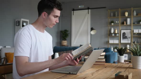 Young Man Reading Book and Working on Laptop