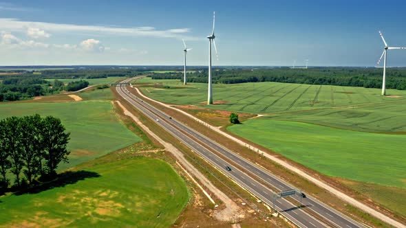 Aerial view of golden field and wind turbines near highway.