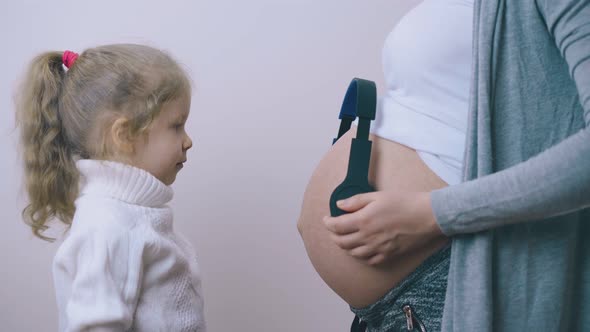 Funny Girl Puts Head on Pregnant Mommy Tummy with Headphones