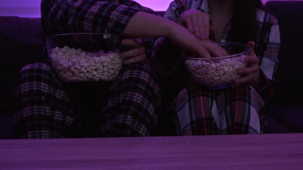 Married Couple in Pajamas Sitting in Front of the TV and Eating Popcorn