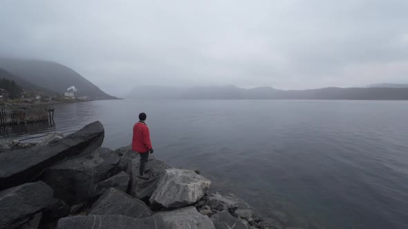 Hiker In Red Looking Out Over Misty Fjord