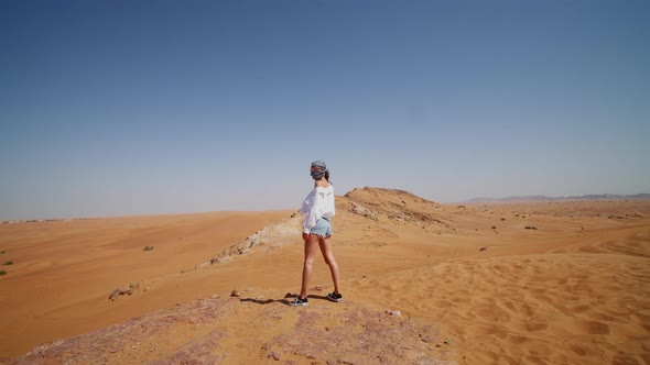 Woman in White Shirt Standing on the Edge of Sand Dune and Looking at the Desert