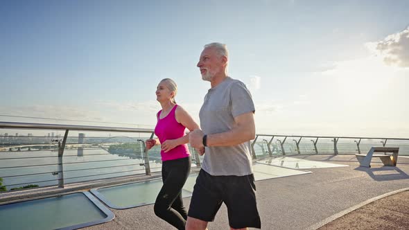 Cheerful Slim Pensioners Enjoy Running in City at Sunrise