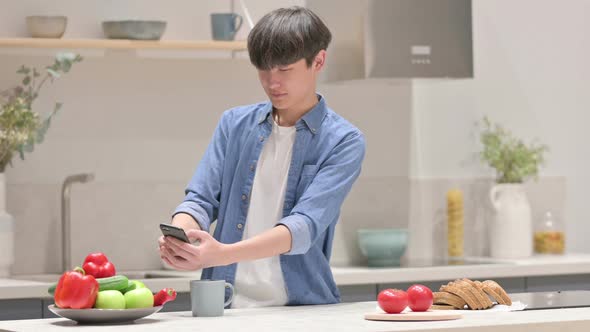 Young Asian Man Taking Picture of Fruits on Smartphone in Kitchen