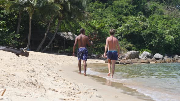 Black and Caucasian Men Walking Together at the Beach on Summer Day.