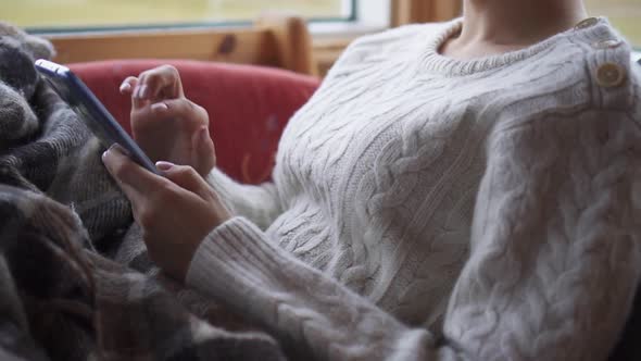 Closeup of Woman Hands Using Smartphone at Home in Comfortable Chair Near Window