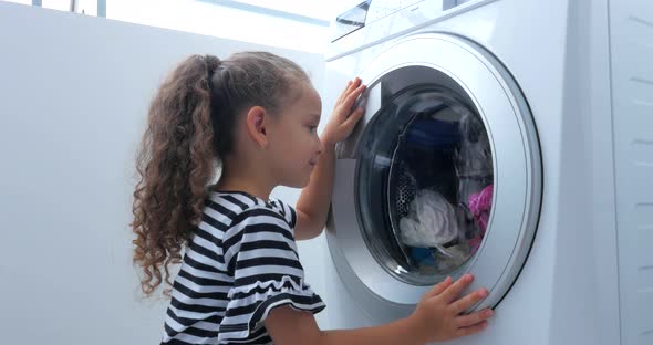 Child Looks Inside the Washing Machine. Cylinder Spinning Machine. Concept Laundry Washing Machine alt