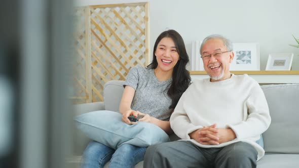 Asian senior father and daughter watch funny movie together at home.