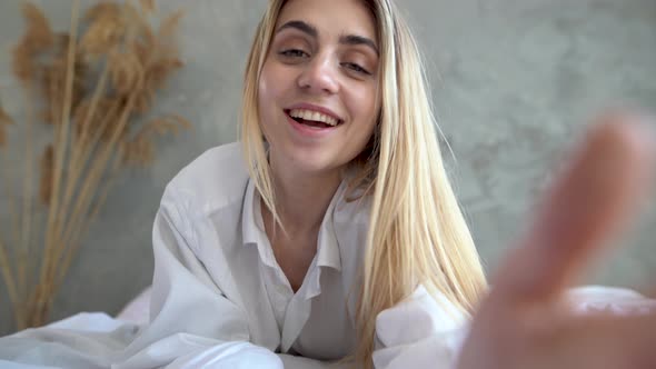 Portrait of Happy Young Caucasian Girl in Casual Clothing Lying Down on Bed While Making Video Call