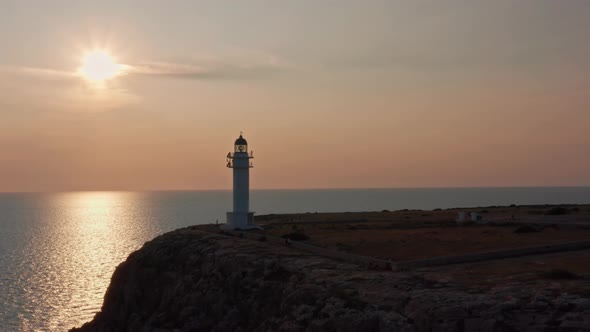 Sun reflected on still sea, white lighthouse on rocky cliff, dolly out