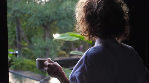 Back Shot of Woman Opening a Window Holding Cup of Coffee