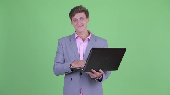 Happy Young Businessman Talking While Using Laptop