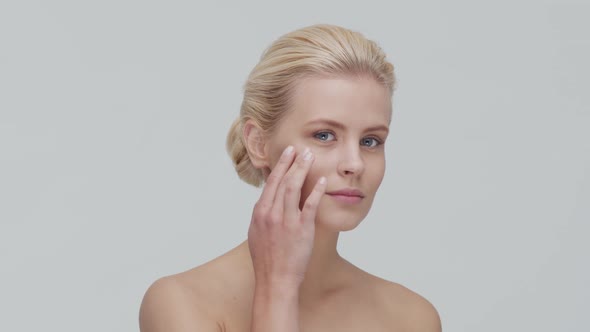 Studio portrait of young, beautiful and natural blond woman applying skin care cream. F