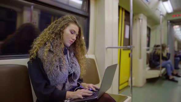 Young Female Student Is Working with Laptop in Metro Train, Sitting and Typing Text