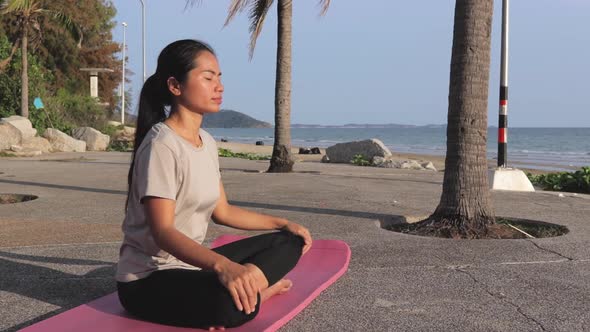 Calm Asian Woman In Casual Sportswear Practicing Yoga By The Shore, Sitting In Lotus Position On A Y