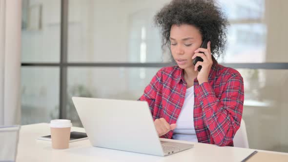 African Woman Talking on Phone While Using Laptop