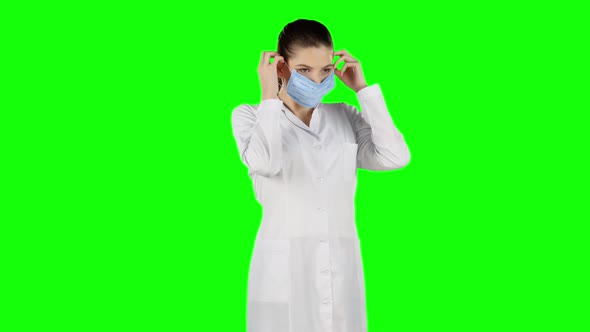 Female Nurse Puts on a Blue Medical Mask. Green Screen
