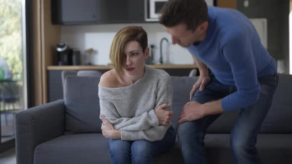 Sad Husband Sitting Down on Couch with Angry Wife Turning Away