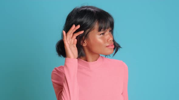 Young Woman Keeps Hand Near Ear Tries To Overhear Something Over Blue Background