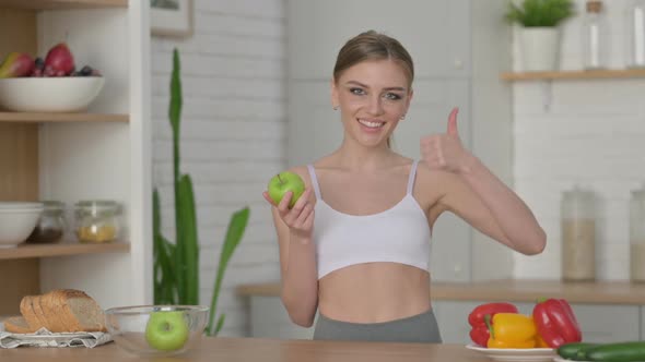 Sporty Woman Showing Thumbs Up While Holding Apple in Kitchen