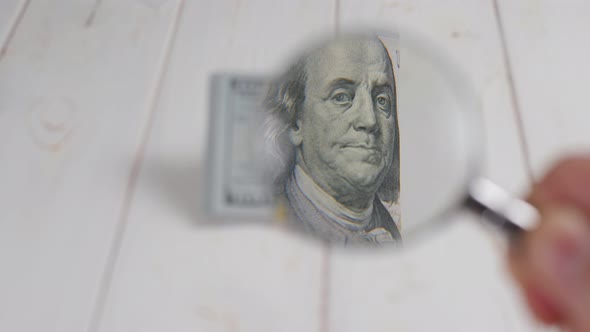 Closeup of a Man Holding a Magnifying Glass to a Hundreddollar Bill