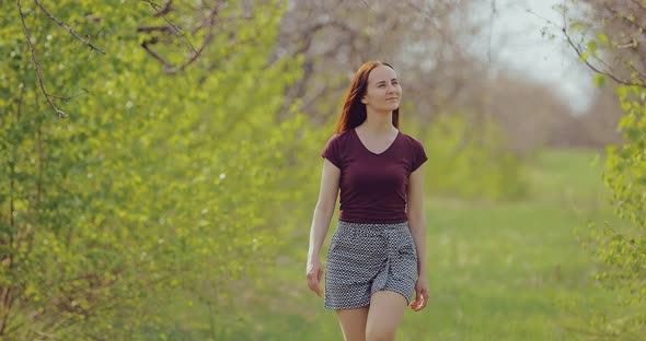 Young Beautiful Woman Walks Along the Trees Through the Forest