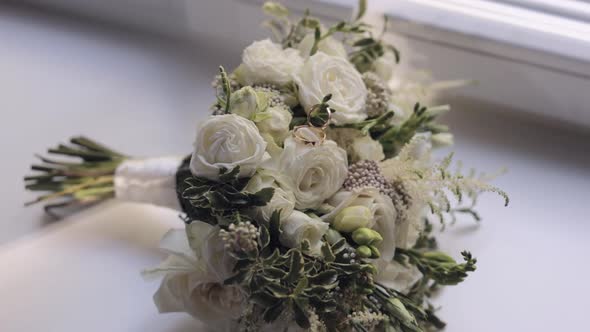 Wedding Golden Rings Lie on Beautiful Wedding White Rose Flowers Bouquet on White Window Sill