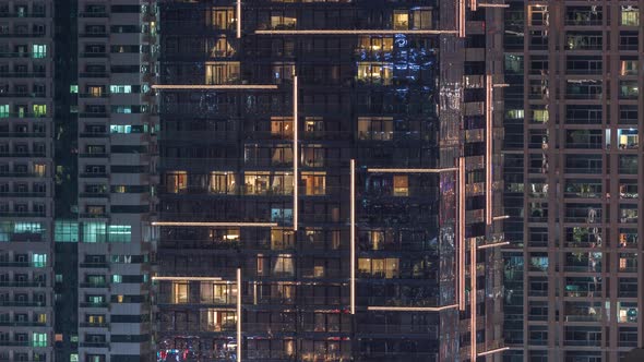 Rows of Glowing Windows with People in Apartment Building at Night