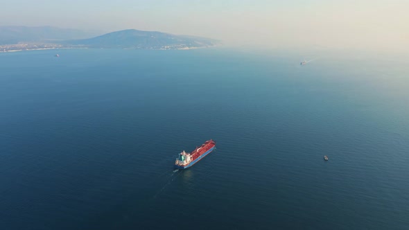 Aerial View Following the Ultra Large Cargo Ship at Sea Leaves Port at Sunset