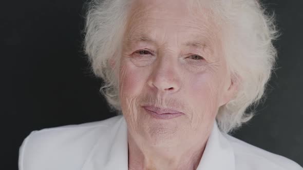 Portrait of Greyhaired Grandmother Talks and Smiles at Camera on Background