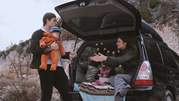 Traveler Family  sitting in the open trunk of a black car with kids near bonfire