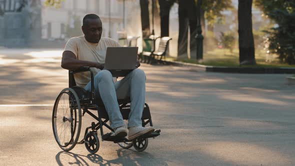 Adult African American Black Man with Disabilities Sitting Outdoors in Summer Park Alone Using