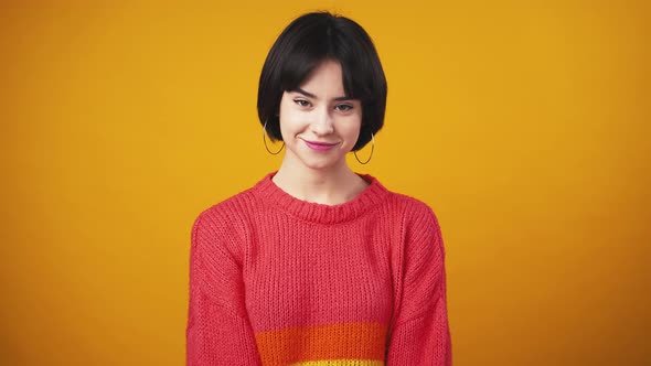 Studio Portrait of Young Cute Woman Wearing Red Sweater Smiling to Camera Orange Background