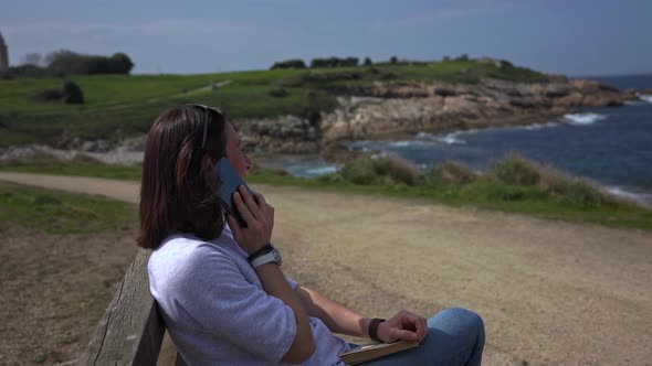 The Girl Talks on the Phone Sitting on a Bench and Looking at the Sea