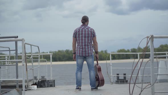 Back View of Carefree Musician Standing on Embankment and Stretching Hands. Wide Shot of Happy