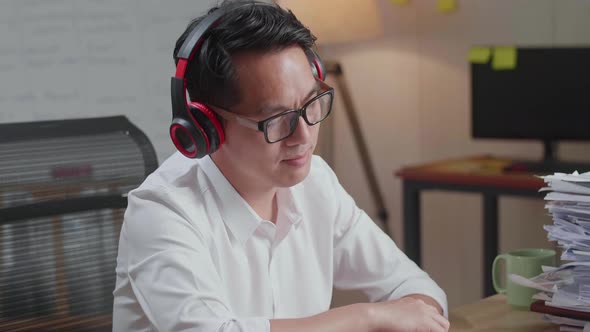 Close Up Of Asian Man Wearing Headphones And Listening To Music After Working With Documents