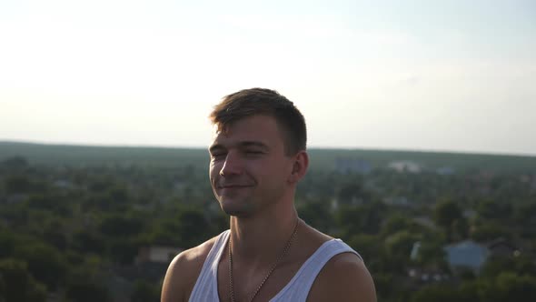 Portrait of Young Happy Man Sitting on Rooftop at Cityscape Background