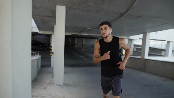 Athlete Runs Around By Levels of an Empty Parking Garage Front View