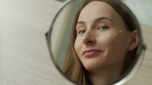 Woman Apply Facial Cream Look in Mirror