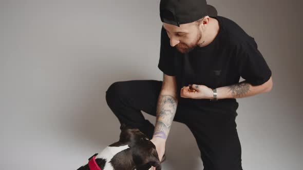 Young Goodlooking Bearded and a Tattooed Man with a Cap Cuddling His Cute Dog Medium Shot Gradient