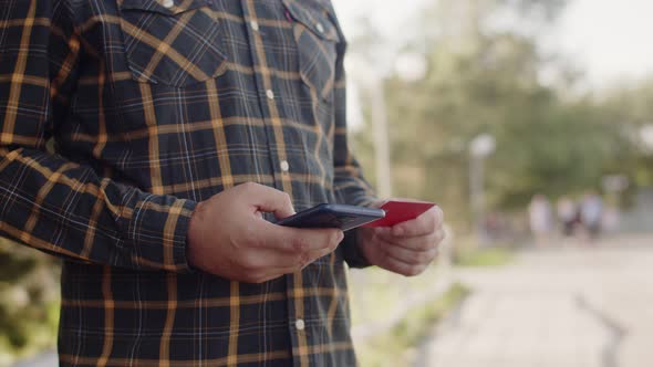 Man holds business bank credit card and dials numbers on mobile phone, front view. Man uses mobile p