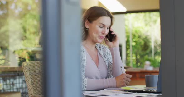 Caucasian pregnant woman sitting at desk, working remotely using smartphone and laptop