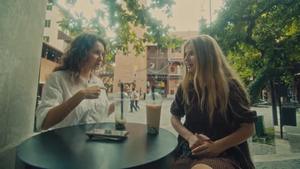 Two Women Sit in a Coffee Shop on the Street and Discuss