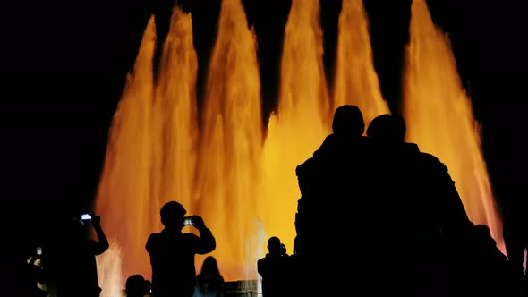 A Lot of Tourists Admire the Huge Orange-lit Fountains in Barcelona