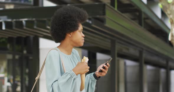 African american businesswoman eating and using smartphone