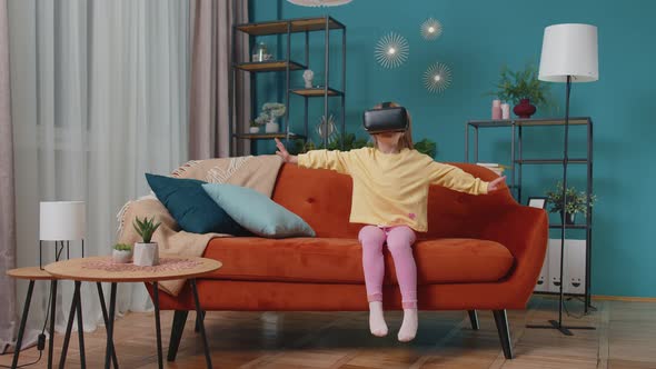 Toddler Girl Sitting on Home Sofa Using Virtual Reality Headset Helmet App to Play Simulation Game