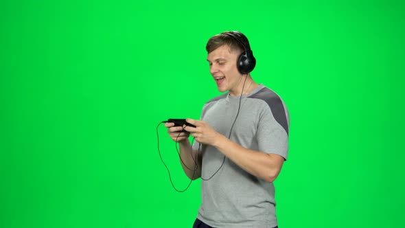 Guy in Big Black Headphones Goes and Texting with Smartphone on Green Screen at Studio